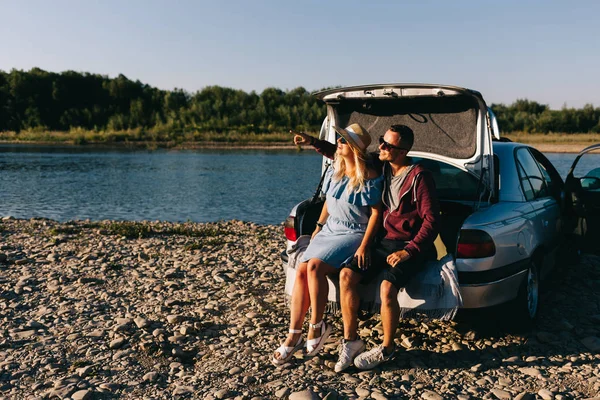 Nöjd resenär par stående nära bil öppna bagageluckan och titta på soluppgången — Stockfoto