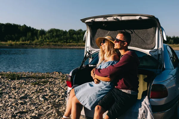 Happy traveler couple standing near car open trunk and watch the sunrise — Stock Photo, Image
