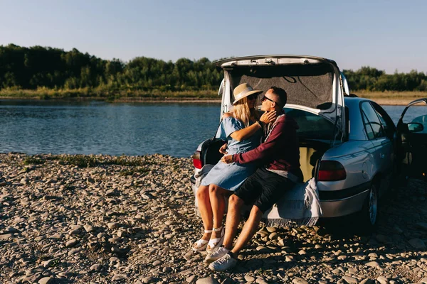 คู่รักนักท่องเที่ยวที่มีความสุขยืนอยู่ใกล้รถเปิดท้ายรถและดูพระอาทิตย์ขึ้น — ภาพถ่ายสต็อก