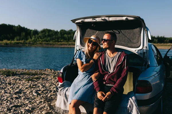 Happy traveler couple standing near car open trunk and watch the sunrise — Stock Photo, Image