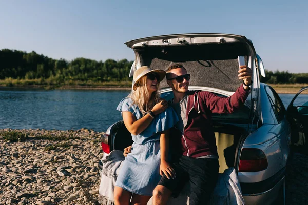 Feliz viajero pareja de pie cerca de coche abierto tronco y ver el amanecer —  Fotos de Stock