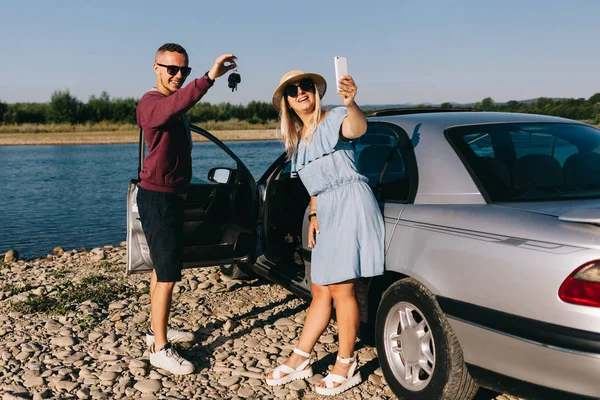 Happy traveler couple standing near car open trunk and watch the sunrise