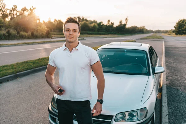 Jovem atraente caucasiano homem em t-shirt branca em pé junto ao carro — Fotografia de Stock