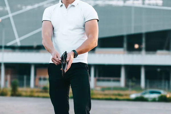 Jovem caucasiano homem de t-shirt branca segura carteira nas mãos — Fotografia de Stock