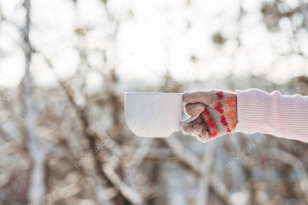 Young girl holds cup of tea in hand in winter park