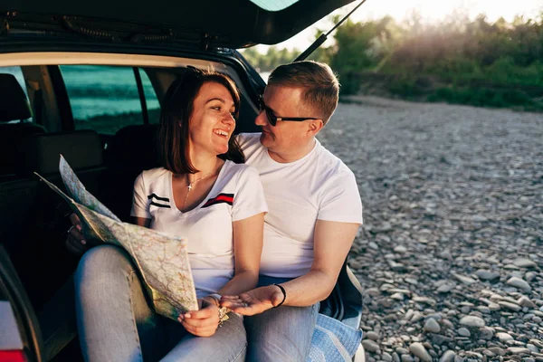 Casal alegre sentado no carro aberto tronco e observando mapa, conceito de viagem — Fotografia de Stock