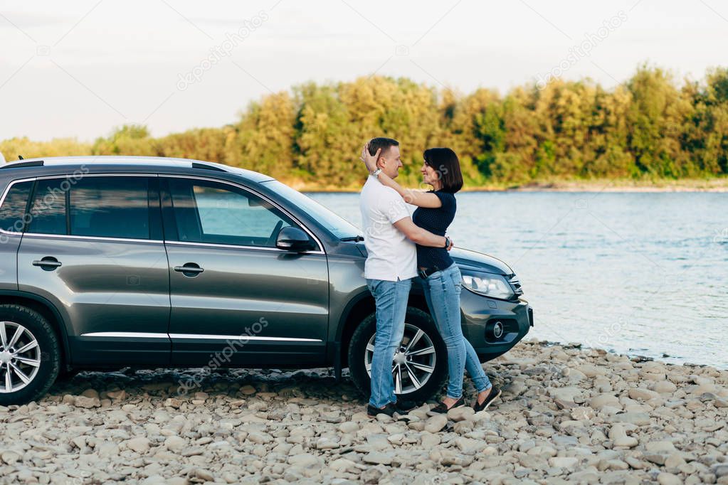 Portrait of happy young adult couple on roadtrip. Man embrace woman near car.