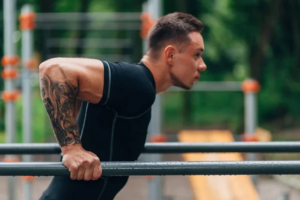 Jovem atleta caucasiano em sportwear preto e tatuagens, treinando ao ar livre e posando — Fotografia de Stock