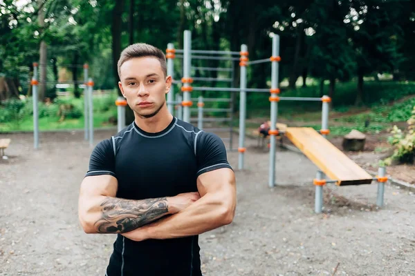 Jonge Kaukasische atleet in zwarte sportwear en tatoeages, opleiding outdoor en poseren — Stockfoto
