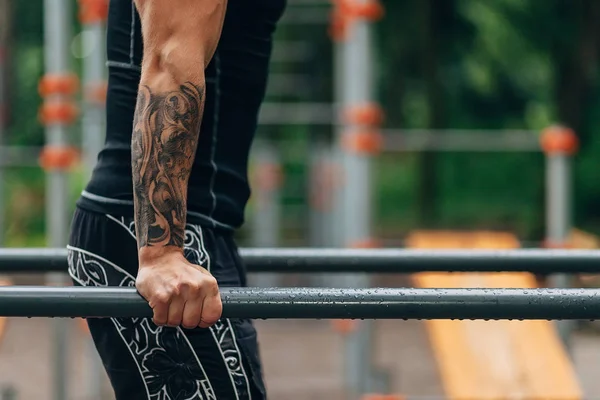 Юный кавказский спортсмен в черной спортивной форме и татуировках, тренируется на открытом воздухе и позирует — стоковое фото