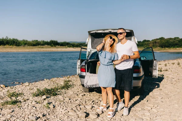 Feliz viajero pareja de pie cerca de coche abierto tronco y ver el amanecer —  Fotos de Stock