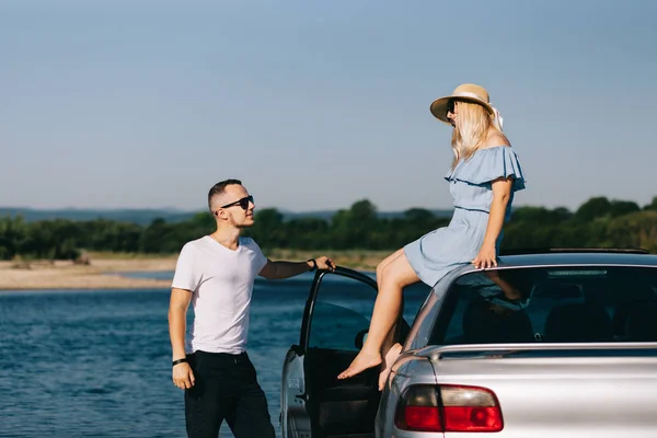 คู่รักนักท่องเที่ยวที่มีความสุขยืนอยู่ใกล้รถเปิดท้ายรถและดูพระอาทิตย์ขึ้น — ภาพถ่ายสต็อก