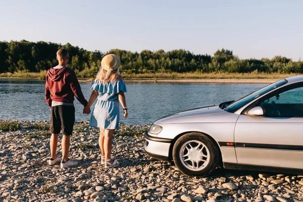 Feliz casal viajante de pé perto do carro aberto tronco e assistir o nascer do sol — Fotografia de Stock