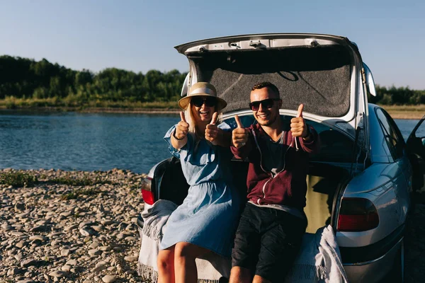 Happy traveler couple standing near car open trunk and watch the sunrise — Stock Photo, Image