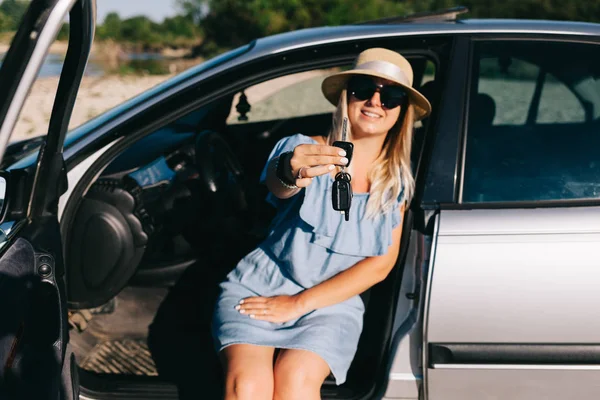 Jovem mulher viajando em um vestido azul está sentado junto ao carro junto ao rio — Fotografia de Stock