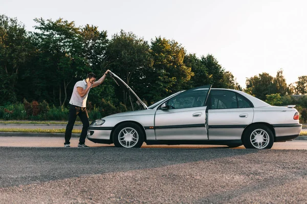 Young attractive caucasian man in white t-shirt standing by the broken car — Stock Photo, Image