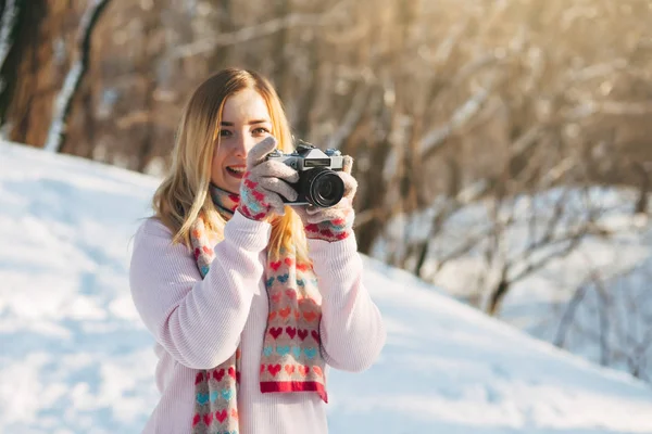Jovem caucasiano atraente menina loira em suéter rosa e cachecol de malha detém câmera de filme retro no parque de inverno ao ar livre — Fotografia de Stock