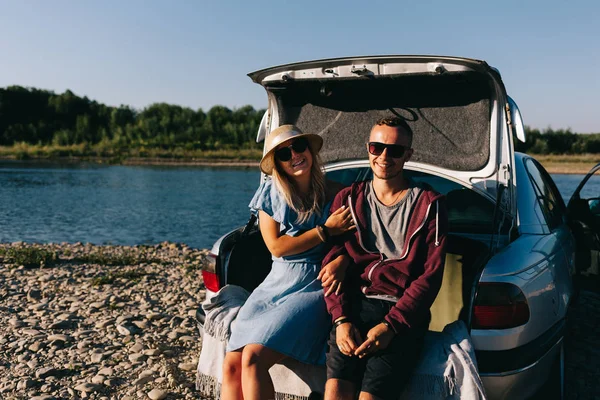 Happy traveler couple standing near car open trunk and watch the sunrise — Stock Photo, Image