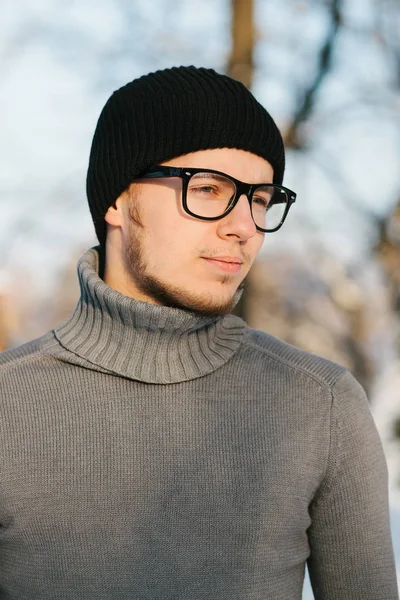 黒い帽子の灰色のセーターで若い男と冬の公園で眼鏡の肖像画 — ストック写真