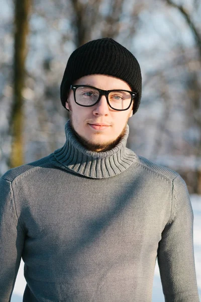黒い帽子の灰色のセーターで若い男と冬の公園で眼鏡の肖像画 — ストック写真