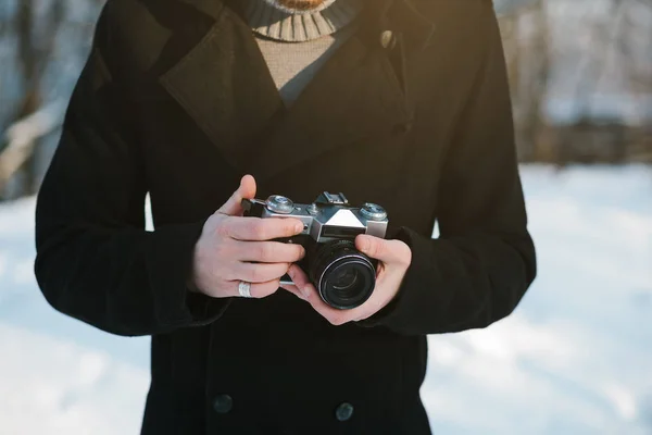 Young man in black coat holds old retro vintage film camera in hands