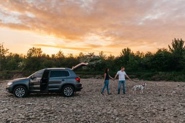 Mutlu genç yetişkin çift ile köpek roadtrip tarihinde portresi. Ekose üzerinde kadınla oturan adam. Açık piknik kavramı.