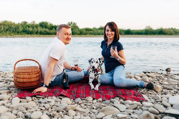 Portrait de couple heureux de jeunes adultes avec chien en voyage. Homme assis sur plaid avec une femme. Concept de pique-nique extérieur . — Photo