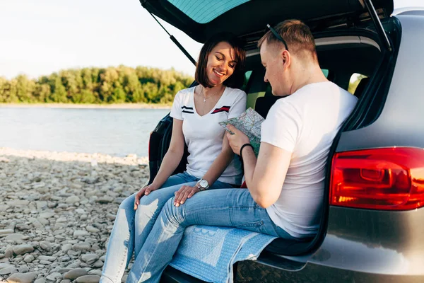 Couple joyeux assis dans le coffre ouvert de voiture et regarder la carte, concept de voyage — Photo