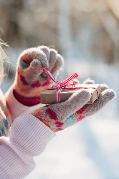 Young woman in knitted gloves unpacks gift in winter park. Close up