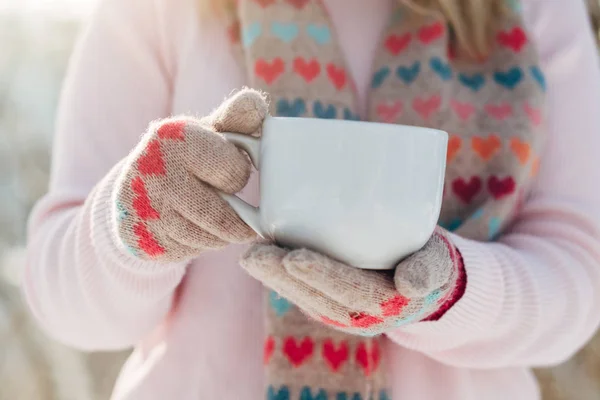 Young girl holds cup of coffe in hands in winter park