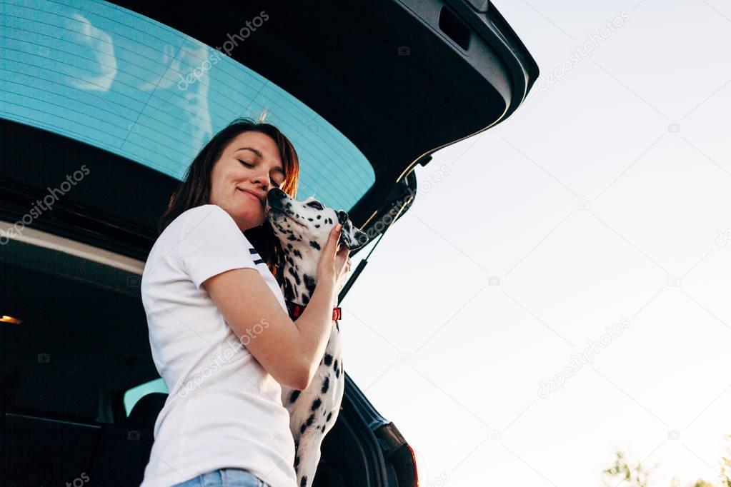 Portrait of cheerful woman sitting in car with dog watching sunset from window, enjoy travel concept.