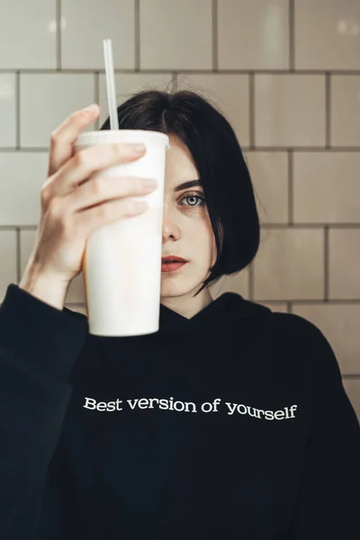 Beautiful Brunette Girl in Black Pullover with Text ''Best Version of Yourself" Holding a Drink — Stock Photo, Image