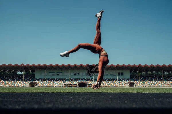 Retrato de una chica deportiva vestida con ropa deportiva de moda haciendo ejercicio y volteretas en el estadio de la ciudad, concepto de estilo de vida saludable — Foto de Stock