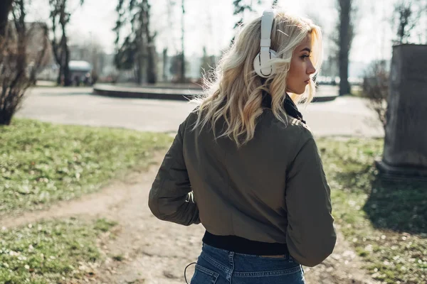 Piękna Blondynka dziewczyna w zielonej kurtki słuchanie muzyki w słuchawkach — Zdjęcie stockowe
