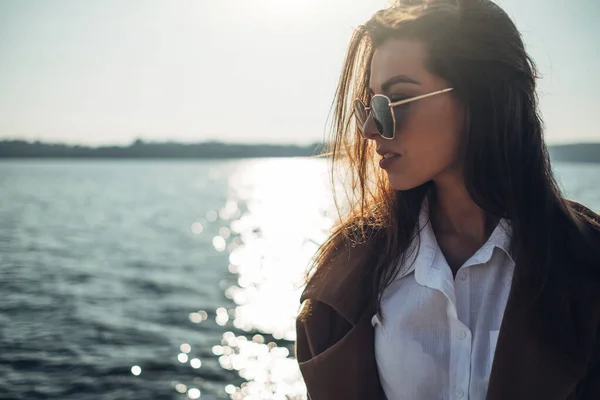 Красива молода стильна дівчина в пальто ходьба на весняному пляжі на заході сонця — стокове фото