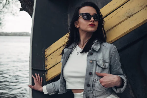 Beautiful Brunette Girl in Sunglasses White Pants and Jeans Jacket Near the Lake — Stock Photo, Image