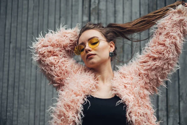 Крупним планом портрет однієї стильної дівчини в рожевому пальто і сучасні жовті сонцезахисні окуляри, що позують на вулиці — стокове фото
