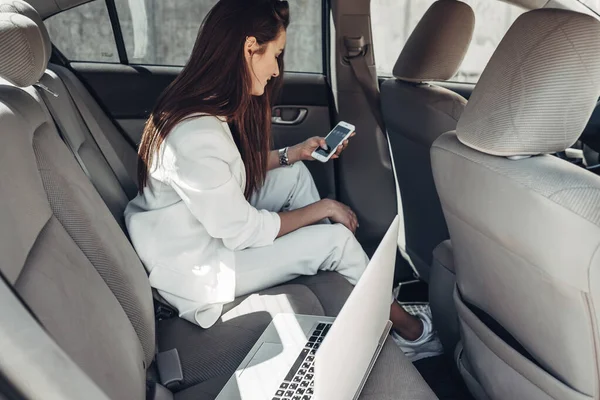 Chica con estilo de moda en traje blanco funciona en el ordenador portátil en el coche — Foto de Stock