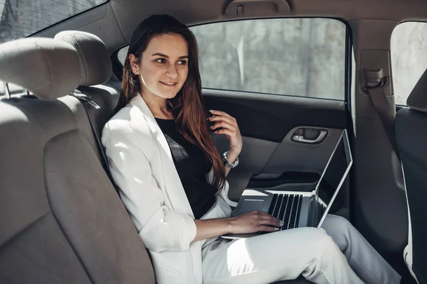 Chica con estilo de moda en traje blanco funciona en el ordenador portátil en el coche — Foto de Stock