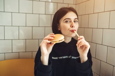 Siyah Kazaklı Güzel Esmer Kız 'En İyi Kendi Versiyonu' ile Lezzetli Bir Burger ve Patates Kızartması Tutuyor