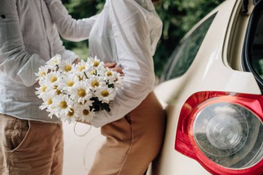 Beyaz tişörtlü genç mutlu çift arabanın yanında eğleniyor, hafta sonu şehir dışında, tatiller ve yolculuk konsepti.