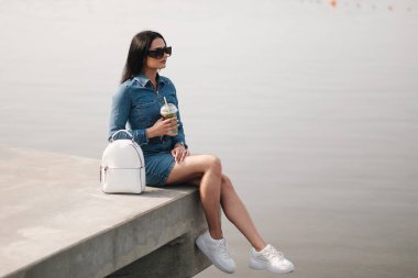 Kot pantolon giymiş güzel bir esmer kız Tulum giyiyor Kokteyl içiyor