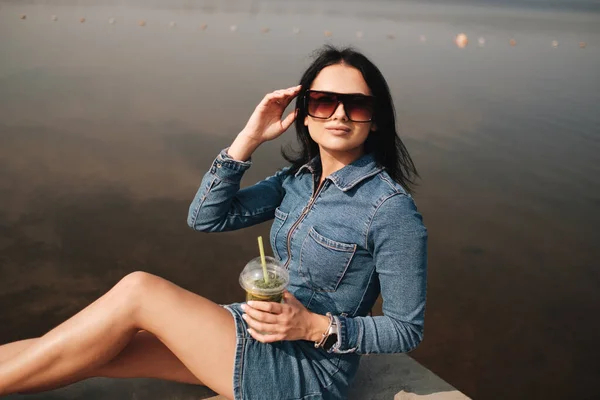 One Beautiful Brunette Girl Dressed in Jeans Overalls Drinks Cocktail — Stockfoto