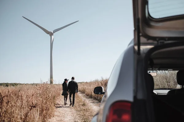 Casal viajante feliz desfrutando de uma viagem de carro na estrada de campo com gerador de energia elétrica turbina eólica no fundo — Fotografia de Stock