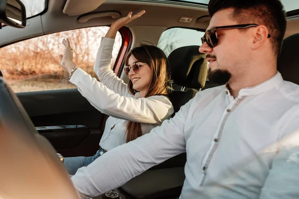 Joven pareja feliz vestida como en camisa blanca y pantalones vaqueros disfrutando de un viaje por carretera en su nuevo coche, hermoso atardecer en el campo, vacaciones y concepto de viaje —  Fotos de Stock