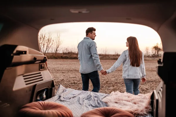 Jong gelukkig paar gekleed als in wit shirt en jeans zitten aan hun nieuwe auto runk, mooie zonsondergang op het veld, vakantie en reizen concept — Stockfoto