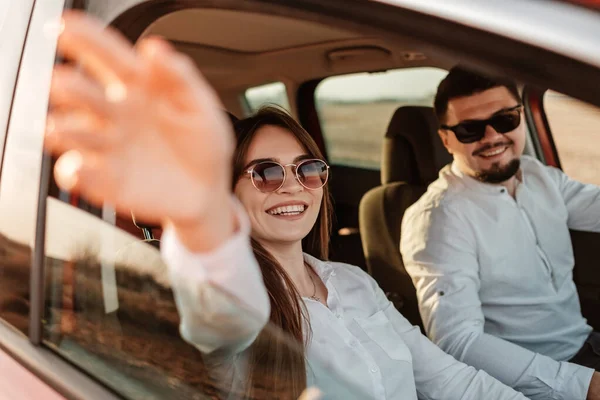 Joven pareja feliz vestida como en camisa blanca y pantalones vaqueros disfrutando de un viaje por carretera en su nuevo coche, hermoso atardecer en el campo, vacaciones y concepto de viaje —  Fotos de Stock