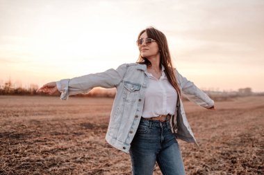 Beyaz gömlekli ve kot ceketli güzel bir kızın portresi, Sunset 'te şehrin dışında iyi vakit geçiriyor.