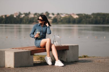 Kot pantolon giymiş güzel bir esmer kız Tulum giyiyor Kokteyl içiyor