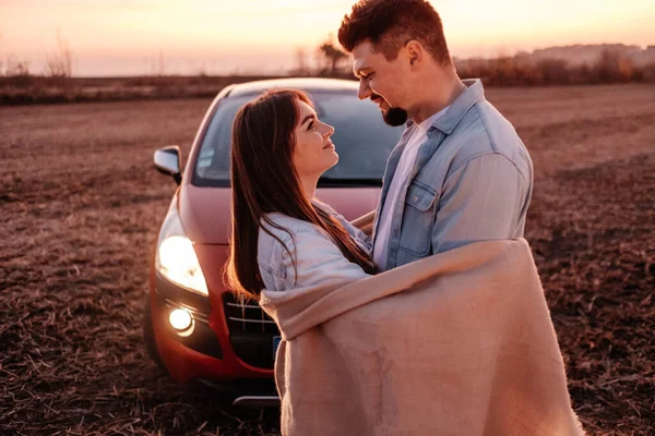 Joven pareja feliz vestida como en camisa blanca y pantalones vaqueros disfrutando de un viaje por carretera en su nuevo coche, hermoso atardecer en el campo, vacaciones y concepto de viaje —  Fotos de Stock